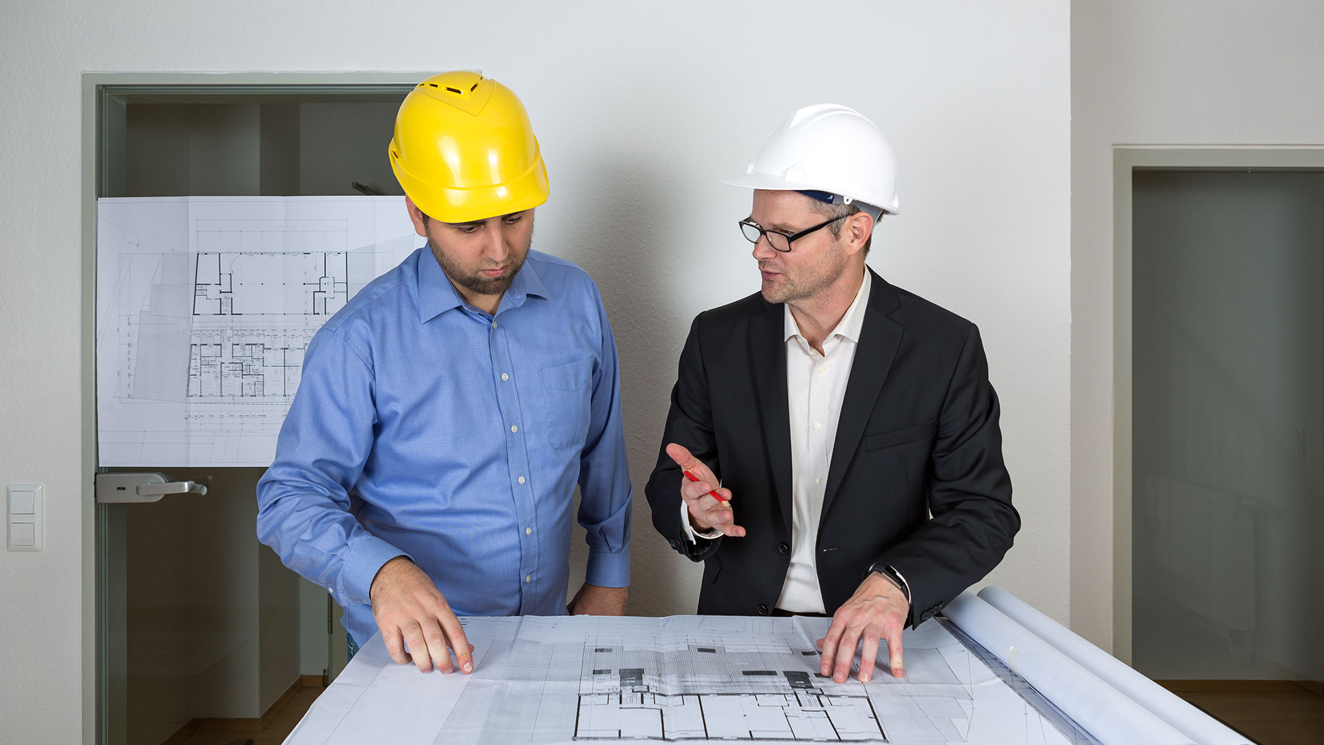 Der Architekt erklärt dem Bauherren Details des Bauplans und zeigt ihm die Planbereiche.